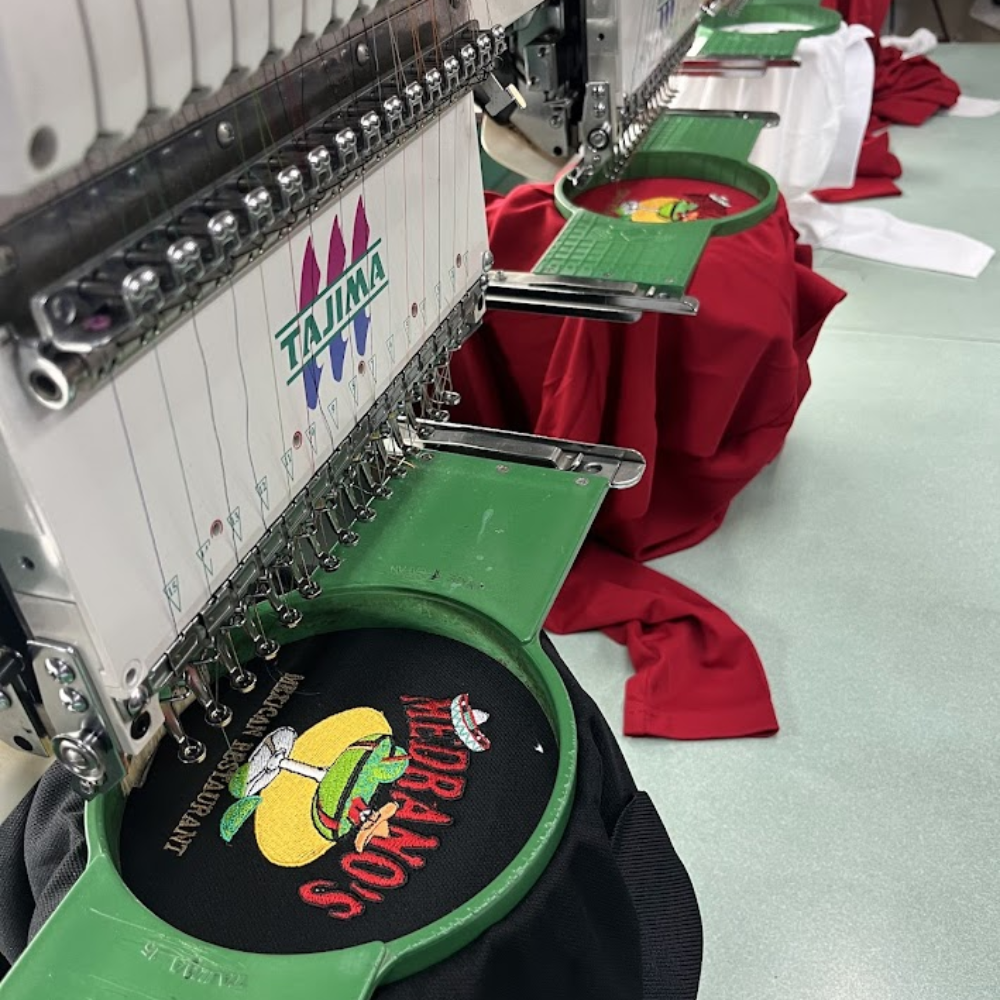 Tajima embroidery machines stitching a custom restaurant logo onto a black garment