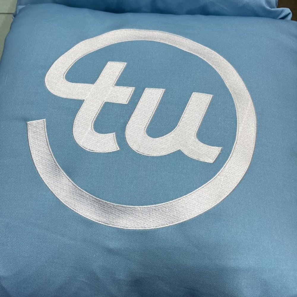 Large white embroidered TU monogram on blue fabric